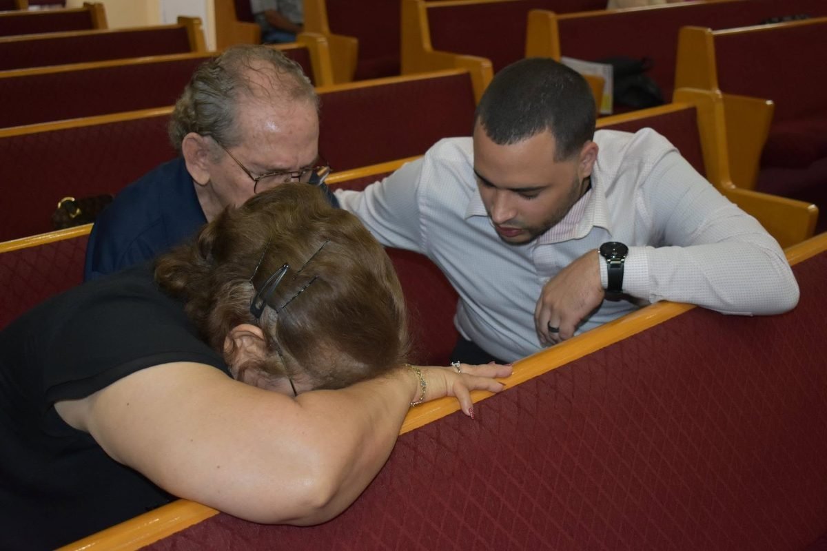 Joven orando junto a una persona mayor en un banco de la iglesia